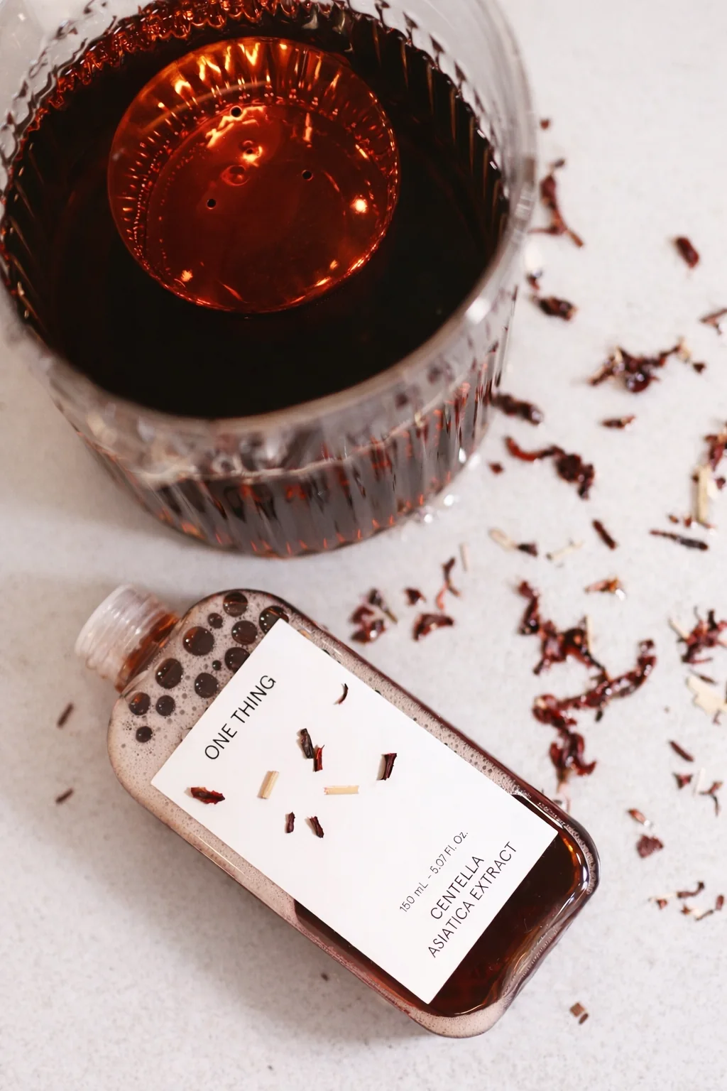 Styled product photo with a body-care jar and phone on a textured surface