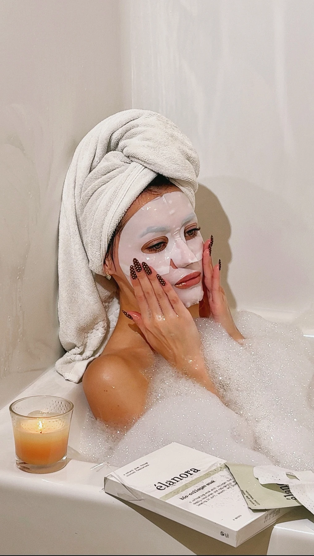 Olesia wearing an élanora sheet mask in a candlelit bubble bath